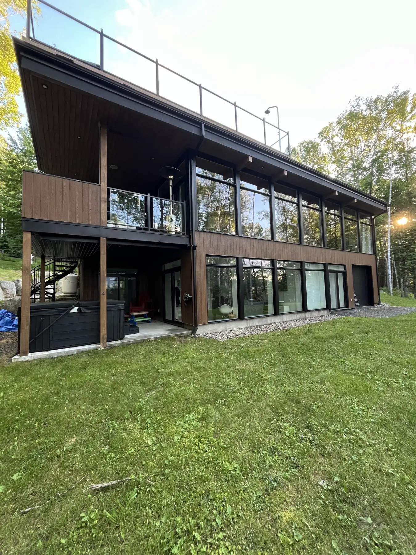 Chalet contemporain en bois entouré d'arbres, avec un mur de fenêtres sur deux étages